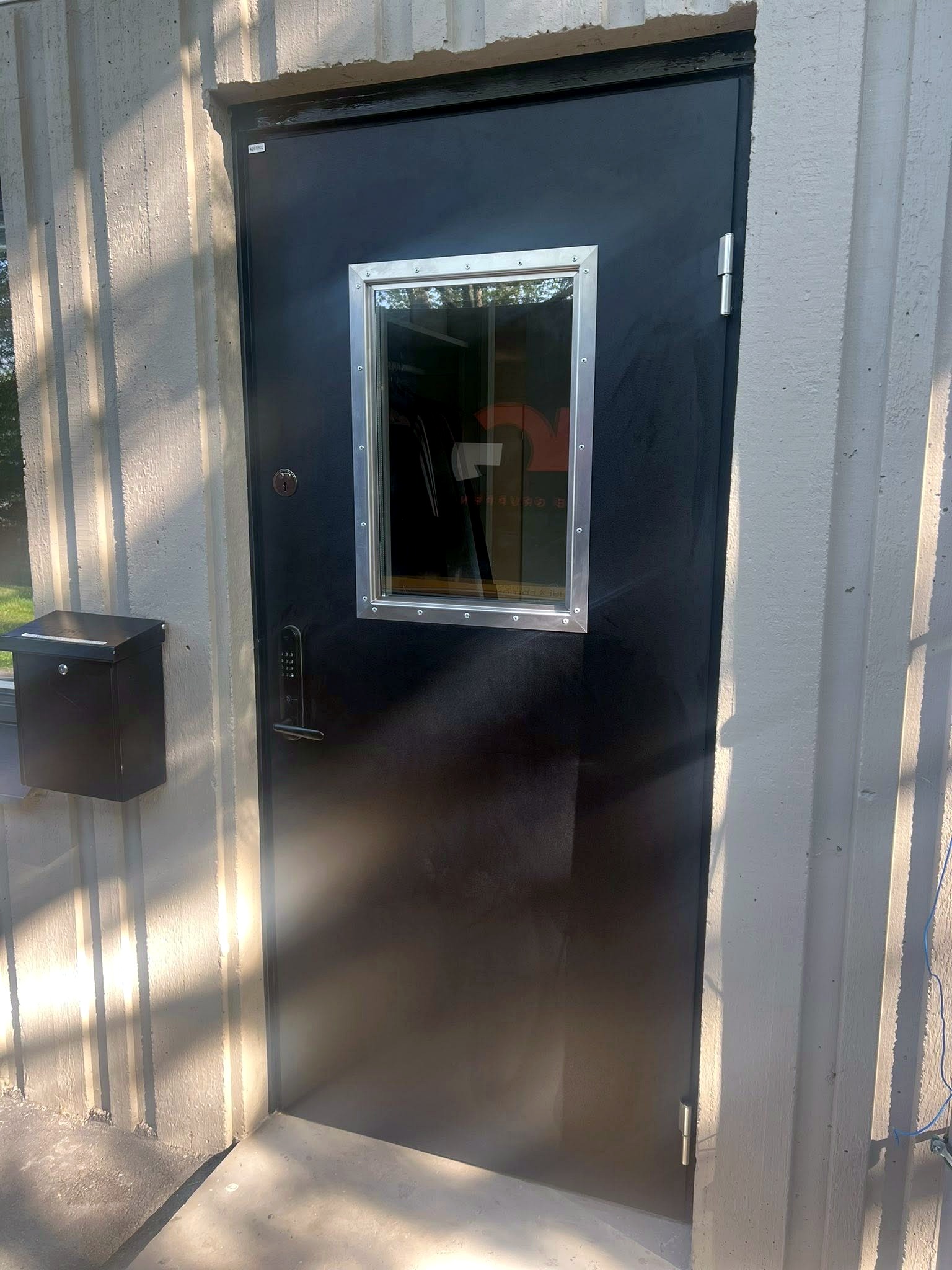 Monterad svart säkerhetsdörr med glasparti i betongvägg